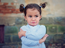 A toddler standing by herself, pouting with her arms crossed